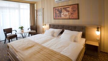 A hotel room with a large bed, two bedside tables, a chair, a small table with a plant, and a wall-mounted air conditioner.