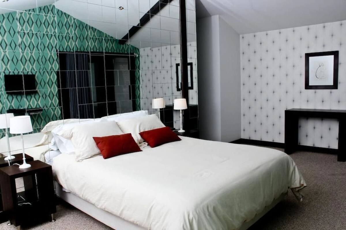 A hotel room with a large bed, two bedside tables with lamps, a green patterned wall, a mirror, and a framed picture on the wall.