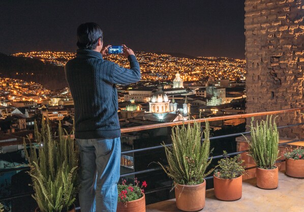 A person taking a photo of a cityscape at night with illuminated buildings and a prominent dome structure. - Hotel Casa Gardenia (Quito)