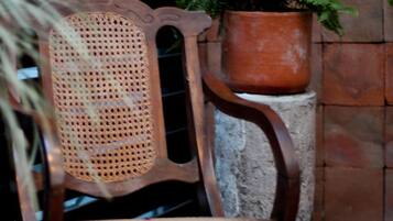 Una silla de madera con respaldo tejido y un helecho en maceta a su lado.