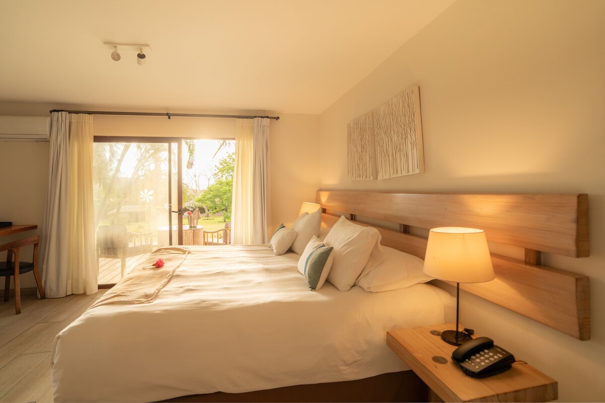 A hotel room with a bed, a desk, a lamp, and a view of the outdoors.