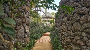 Un sendero de piedra conduce a una construcción con techo de paja rodeada de abundante vegetación.