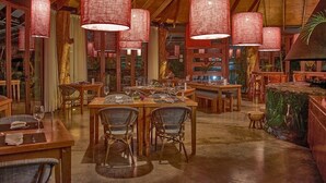 Un restaurante con mesas y sillas de madera, lámparas colgantes rojas y un mural tropical en la pared.