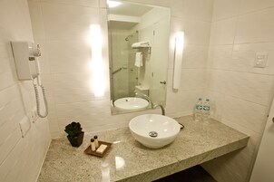 A bathroom with a white sink, a mirror, a hairdryer, and two bottles of water.