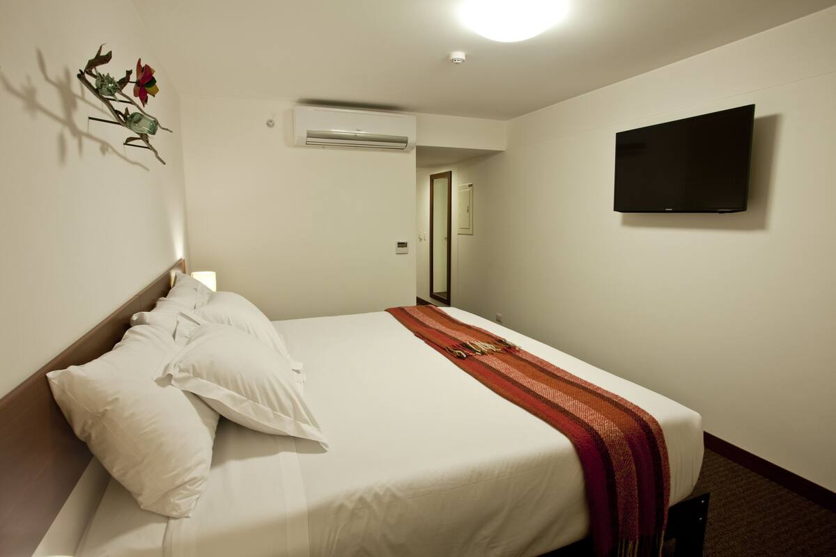 Une chambre d’hôtel équipée d’un lit, d’oreillers, d’une couverture, d’un appareil de climatisation, d’un téléviseur à écran plat et d’une porte donnant sur une autre pièce.