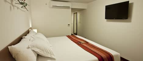 Une chambre d’hôtel équipée d’un lit, d’oreillers, d’une couverture, d’un appareil de climatisation, d’un téléviseur à écran plat et d’une porte donnant sur une autre pièce.
