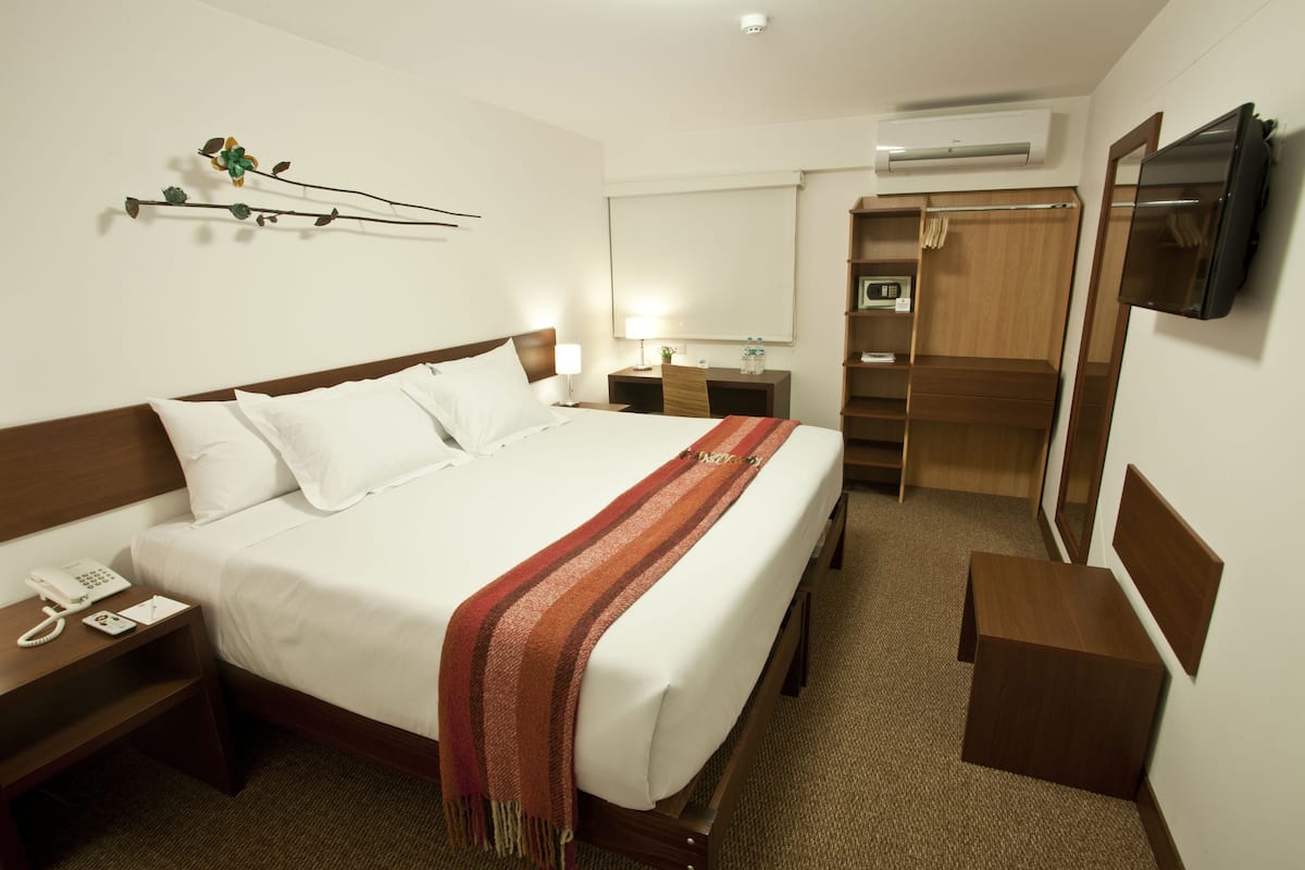 Une chambre d’hôtel comprenant un lit, une table de chevet avec un téléphone, une commode, une lampe, une télévision, une armoire et un miroir.