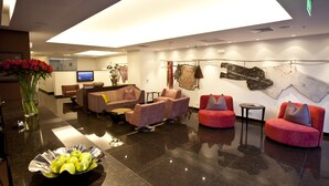 Un hall d’entrée moderne doté d’un haut plafond, d’un téléviseur à écran plat et de différents types de sièges, notamment des canapés et des fauteuils.