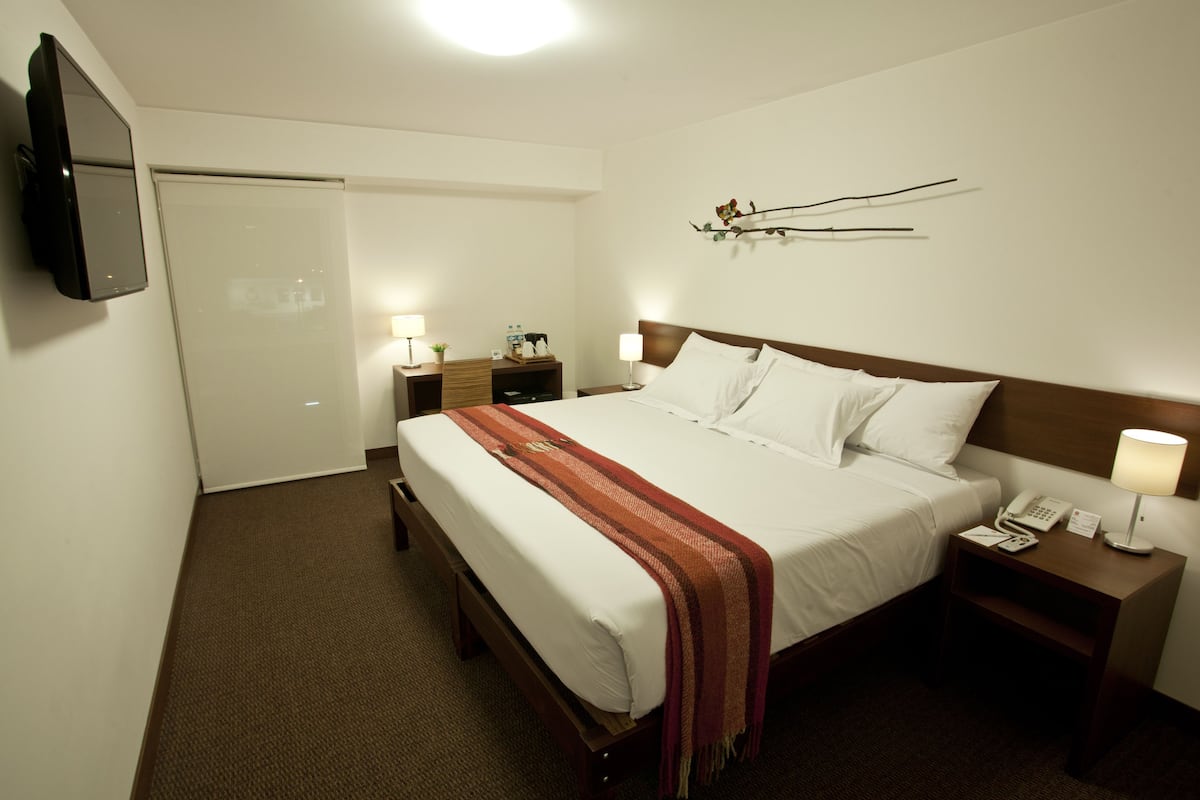 Une chambre d’hôtel comprenant un lit, des tables de chevet, un téléviseur et une œuvre d’art accrochée au mur.