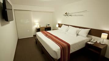 A hotel room with a bed, bedside tables, a TV, and a wall-mounted artwork.