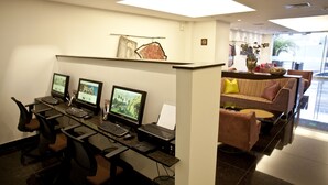 Un espace de bureau moderne avec un grand bureau, plusieurs écrans et des chaises de bureau. On aperçoit un canapé avec des coussins à l’arrière-plan.