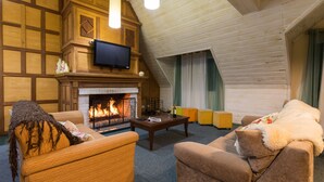 A cozy living room with a fireplace, wooden walls, and a television. - Hotel Parque das Flores (Campos do Jordão)