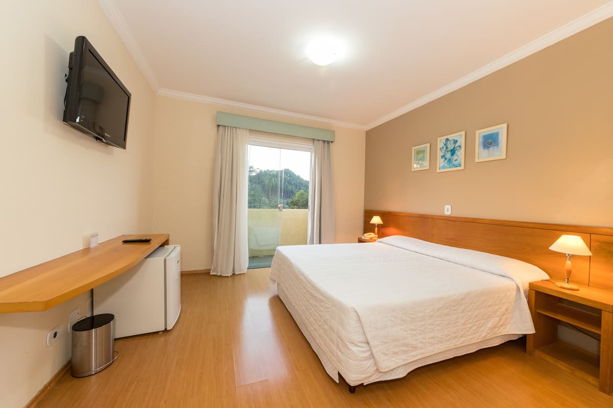 A hotel room with a bed, bedside table, lamp, TV, and a small refrigerator.