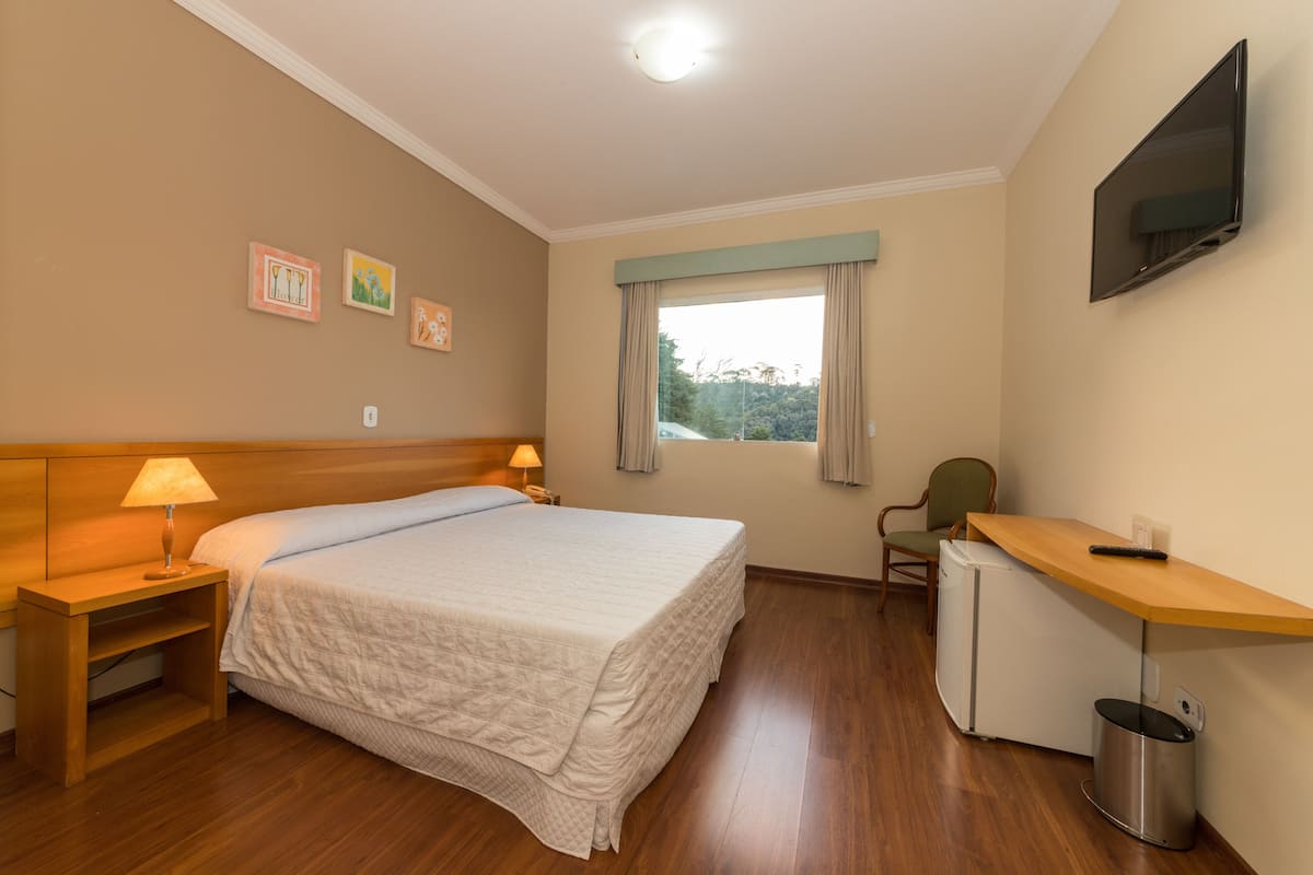 A hotel room with a bed, bedside table, lamp, desk, chair, TV, and a small refrigerator.