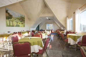 Un comedor con mesas dispuestas para el servicio, un cuadro en la pared y un techo inclinado.