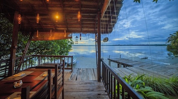 Una terraza de madera con vistas a un lago tranquilo y barcos a lo lejos.