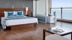 Une chambre d’hôtel moderne avec un grand lit, une lampe de chevet, un téléphone et une vue sur la mer, accessible par une porte-fenêtre coulissante.