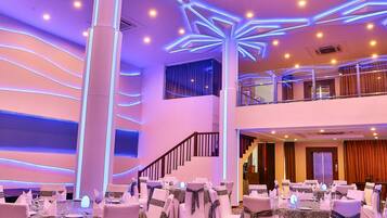 A banquet hall with tables set for events, a central pillar, and a patterned carpet.