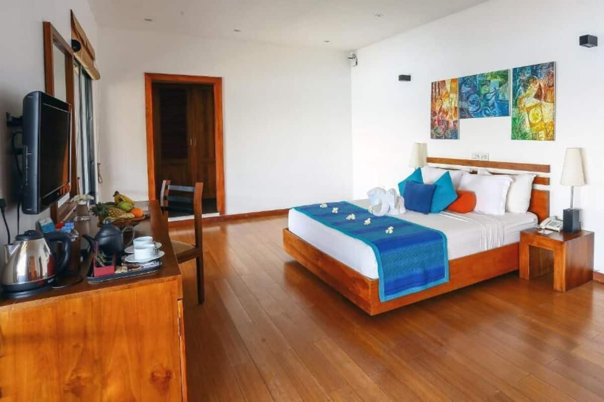 Une chambre avec un lit en bois, une télévision, un bureau avec une bouilloire et une chaise.