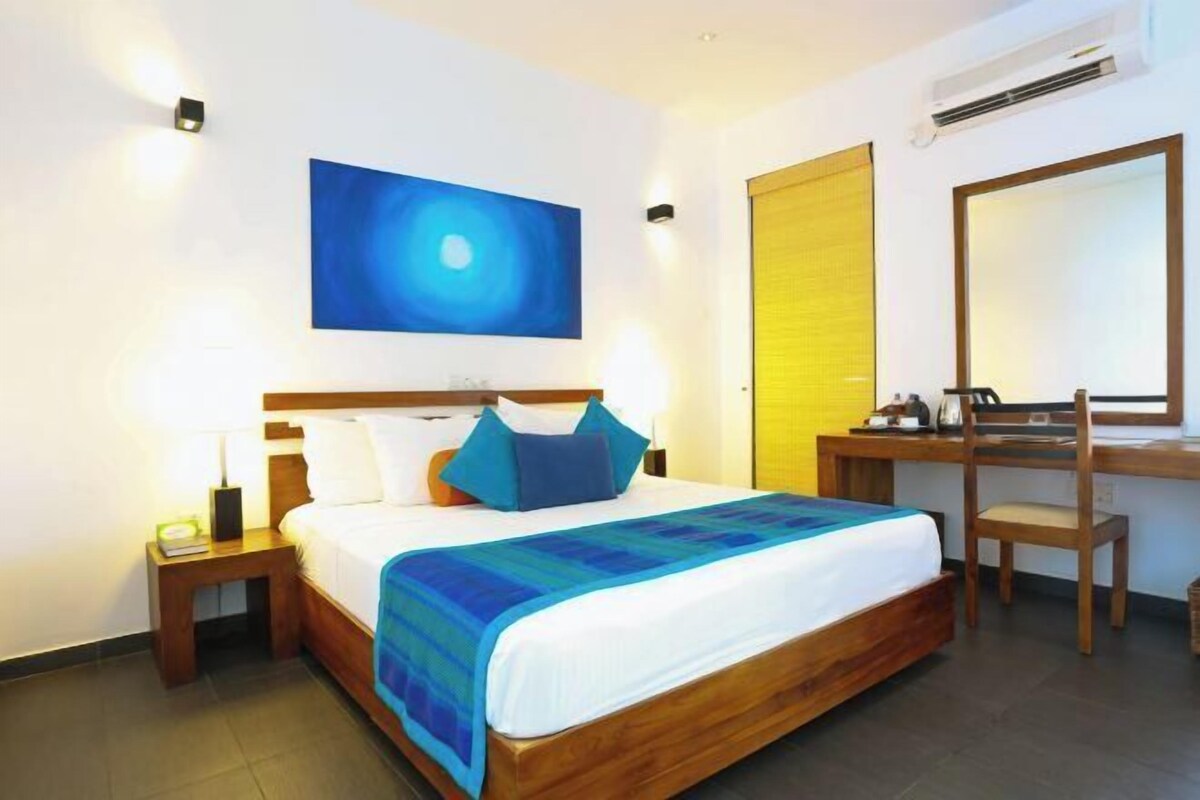Une chambre d’hôtel comprenant un lit, un bureau, une chaise, une table de chevet, un climatiseur fixé au mur et un tableau.