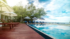 Zona junto a la piscina con sillones de descanso y sombrillas, un muelle de madera y vistas al agua.