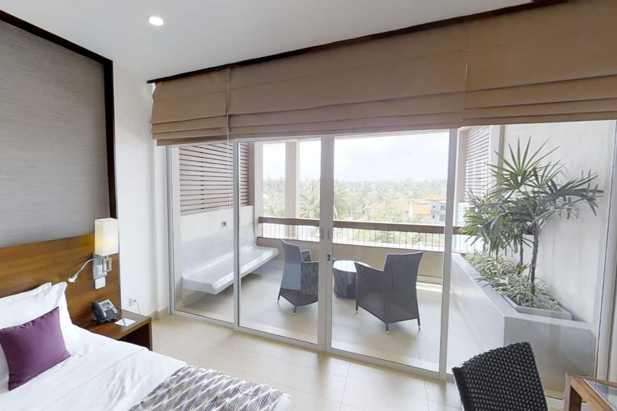 Une chambre d’hôtel comprenant un lit, une table de chevet, une lampe et un balcon avec une table et des chaises.