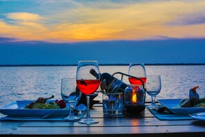 A table set for a meal with wine glasses, a candle, and a plate of food by a waterfront.