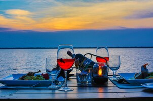 Una mesa lista para una comida, con copas de vino, una vela y un plato de comida frente al agua.