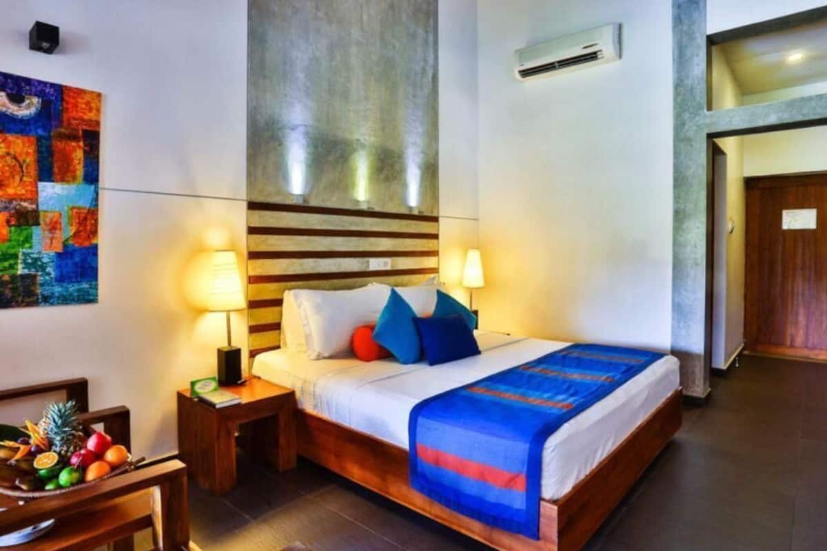 Une chambre d’hôtel avec un lit, des lampes de chevet, un panier de fruits et un tableau au mur.