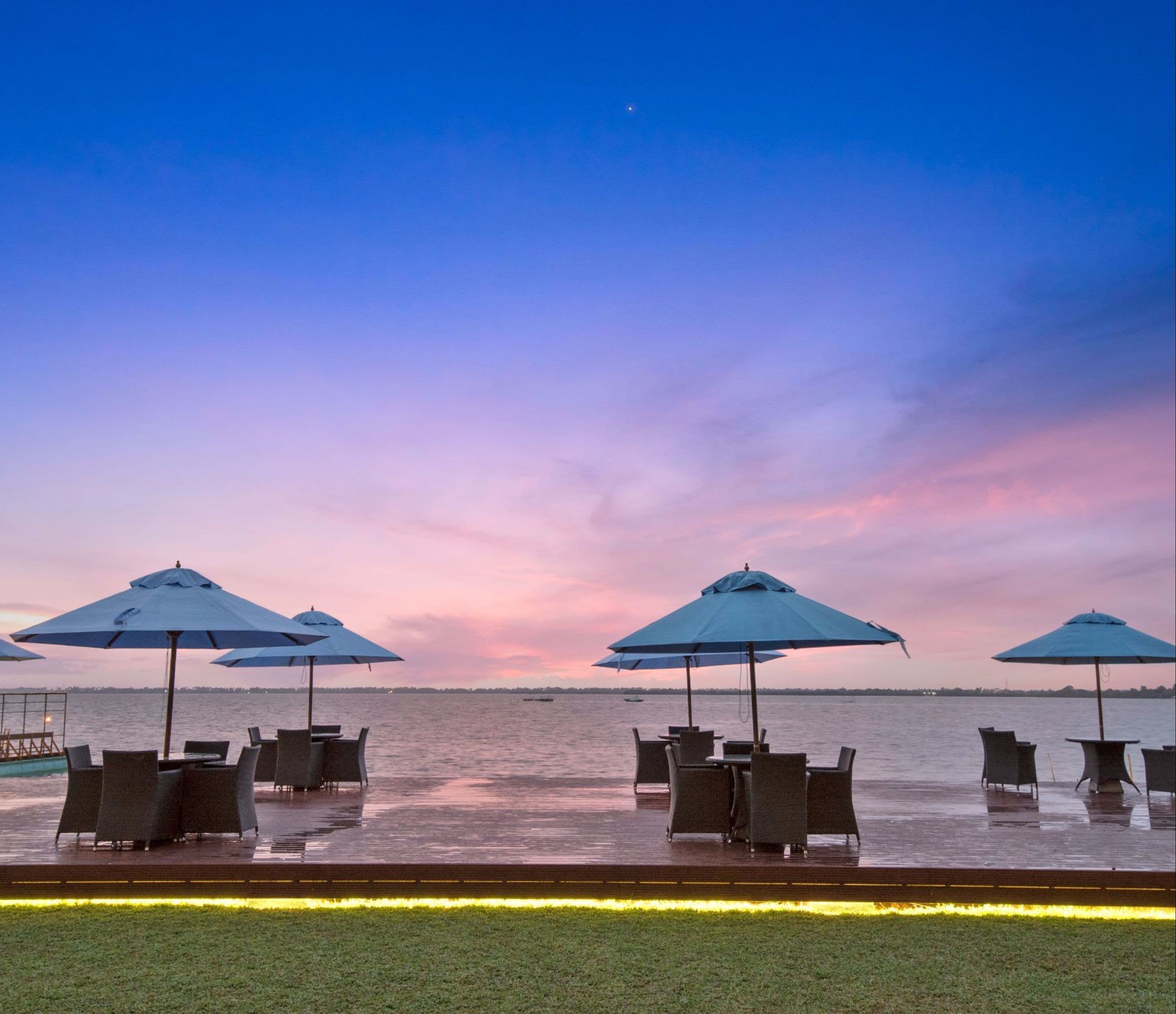 A waterfront terrace with outdoor seating and umbrellas, overlooking a body of water.
