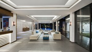 Un hall d’hôtel moderne avec un comptoir d’accueil, un espace salon et une vue sur la piscine.