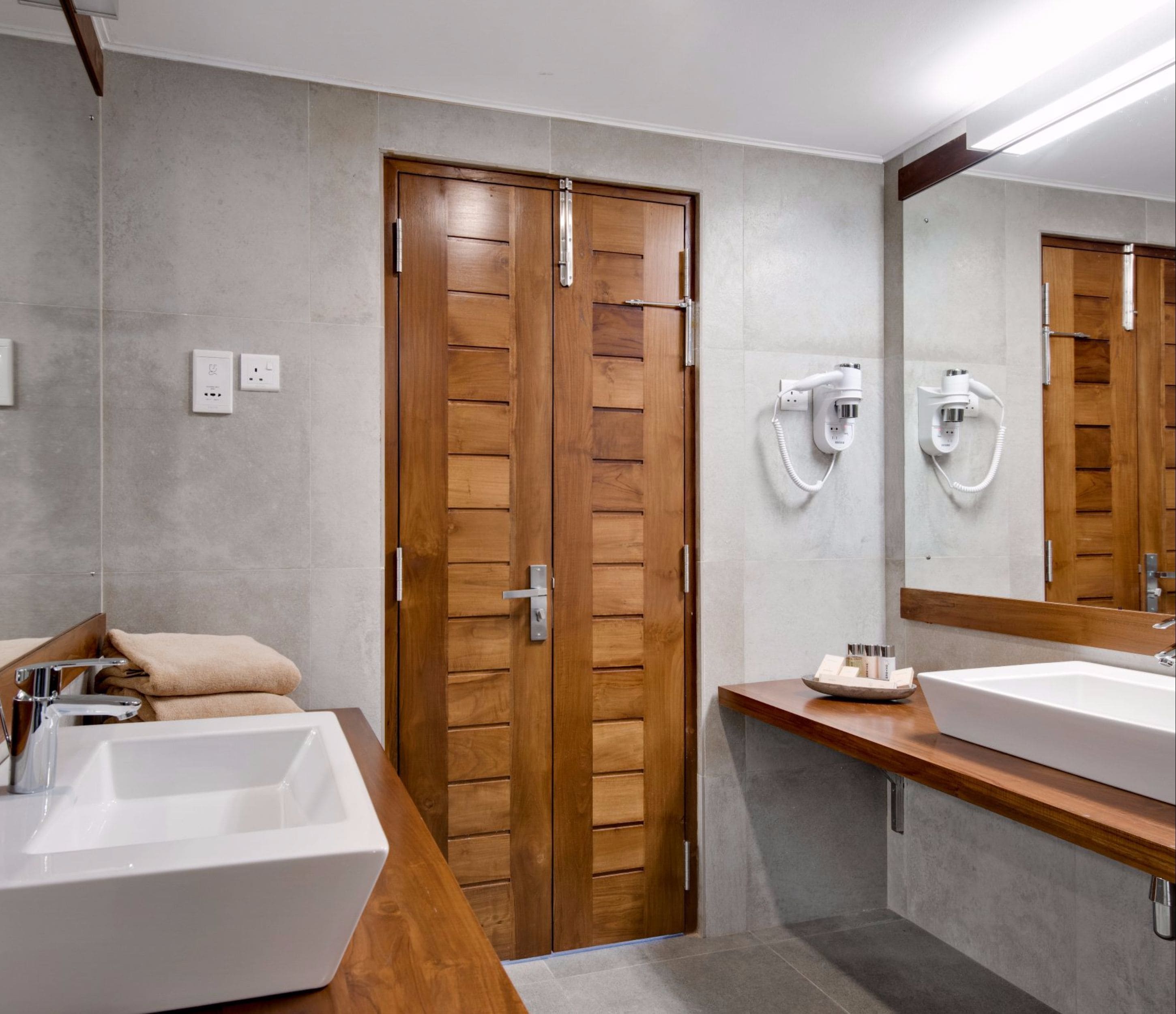Un baño moderno con dos lavamanos, puertas de madera y un espejo grande.