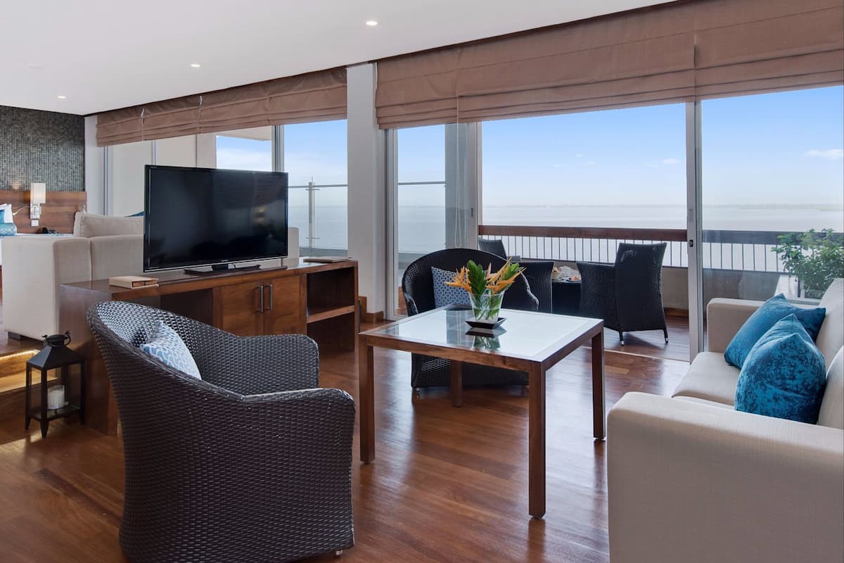 Un vaste espace de vie comprenant un grand téléviseur, des sièges confortables, une table à manger et un balcon avec vue sur la mer.