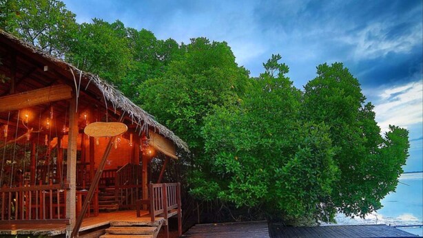 Une structure en bois, dotée d’un toit de chaume et d’une enseigne indiquant « Yale House », jouxtant une terrasse en bois menant à une zone de piscine.