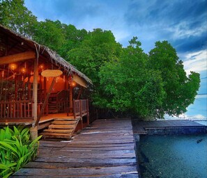 A wooden structure with a thatched roof and a sign reading "Yale House," adjacent to a wooden deck leading to a pool area.