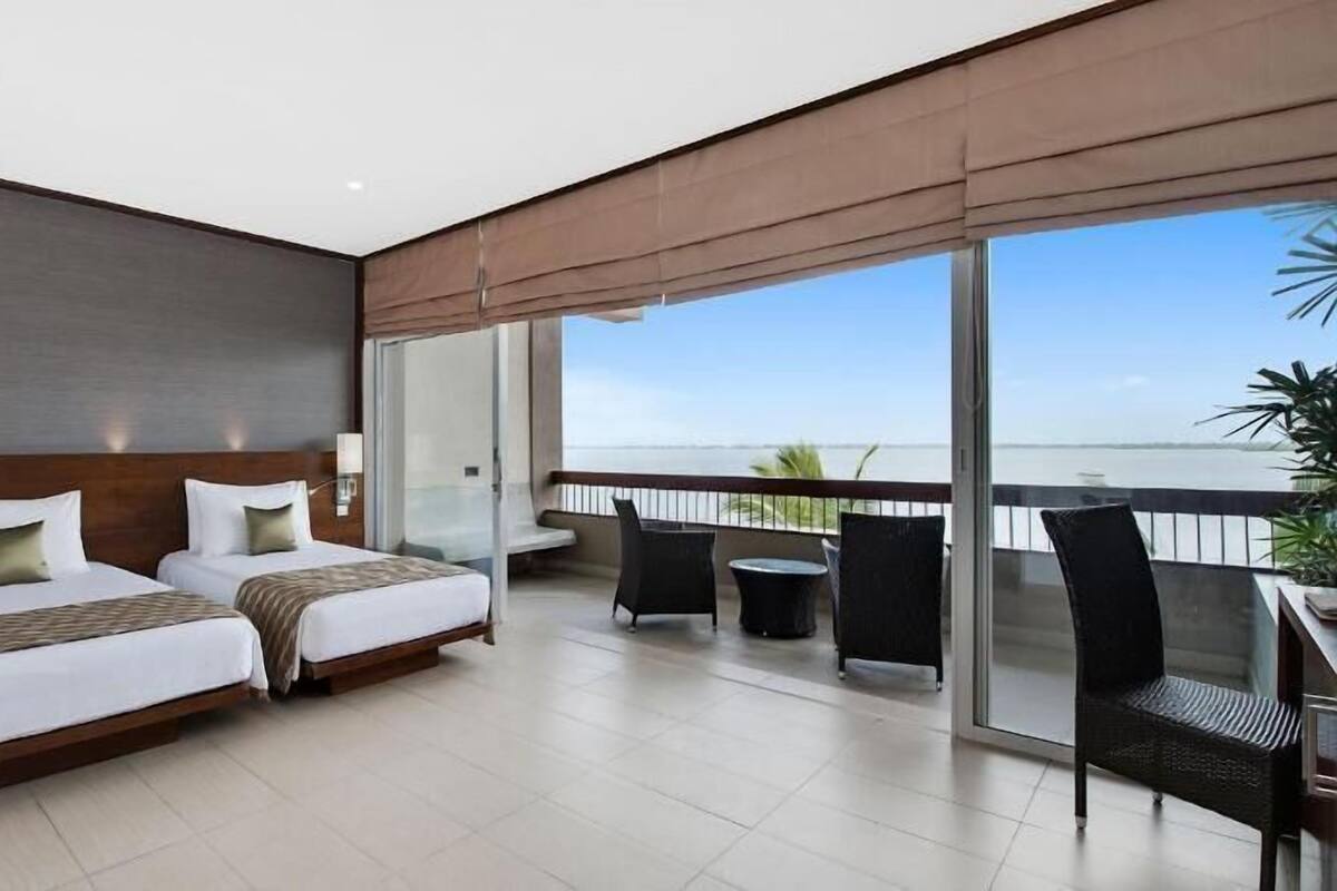 Une chambre d’hôtel avec deux lits, un balcon donnant sur la mer et un coin repas avec des chaises.