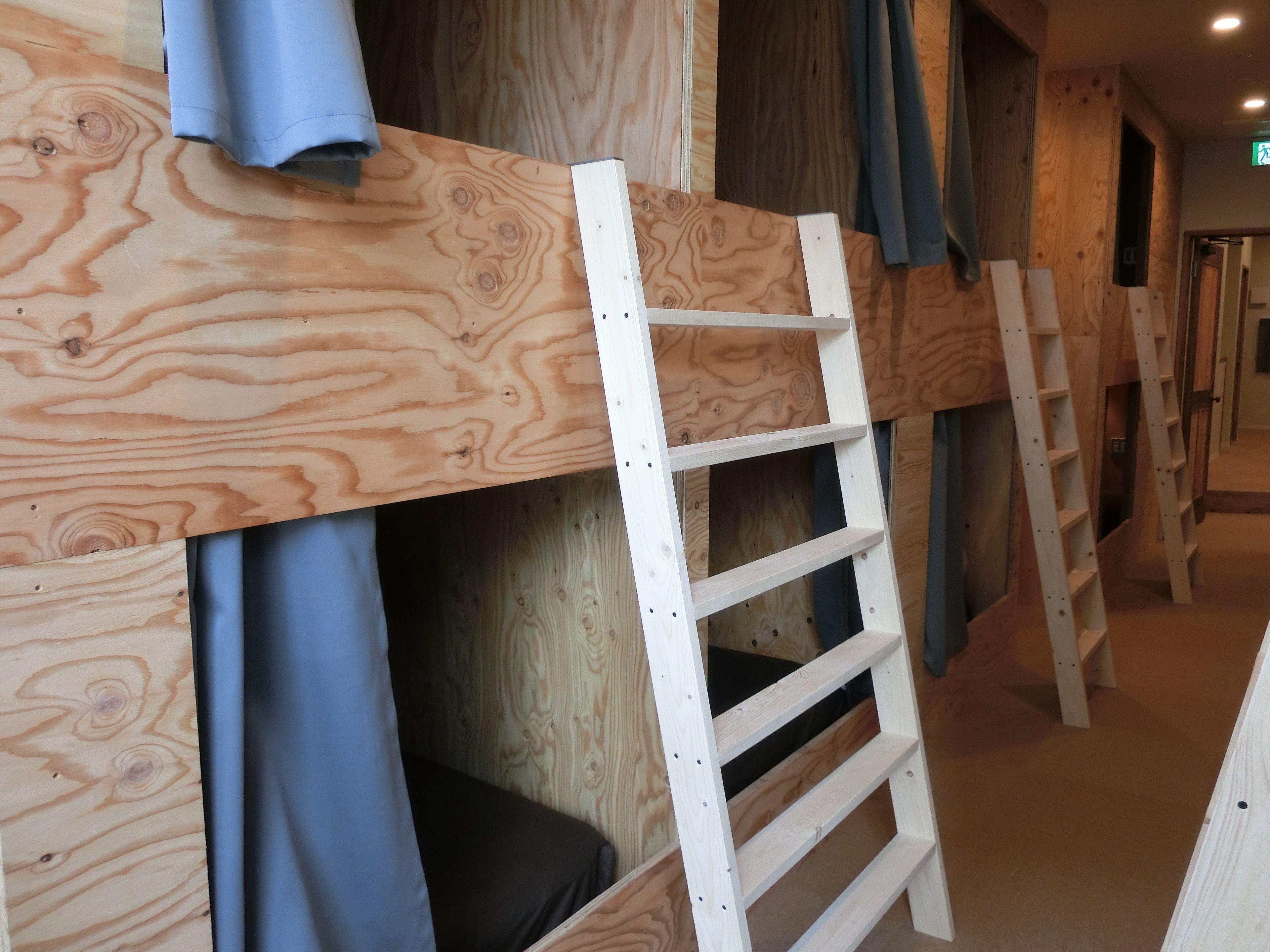 A bunk bed with a ladder, wooden walls, and a blue curtain.