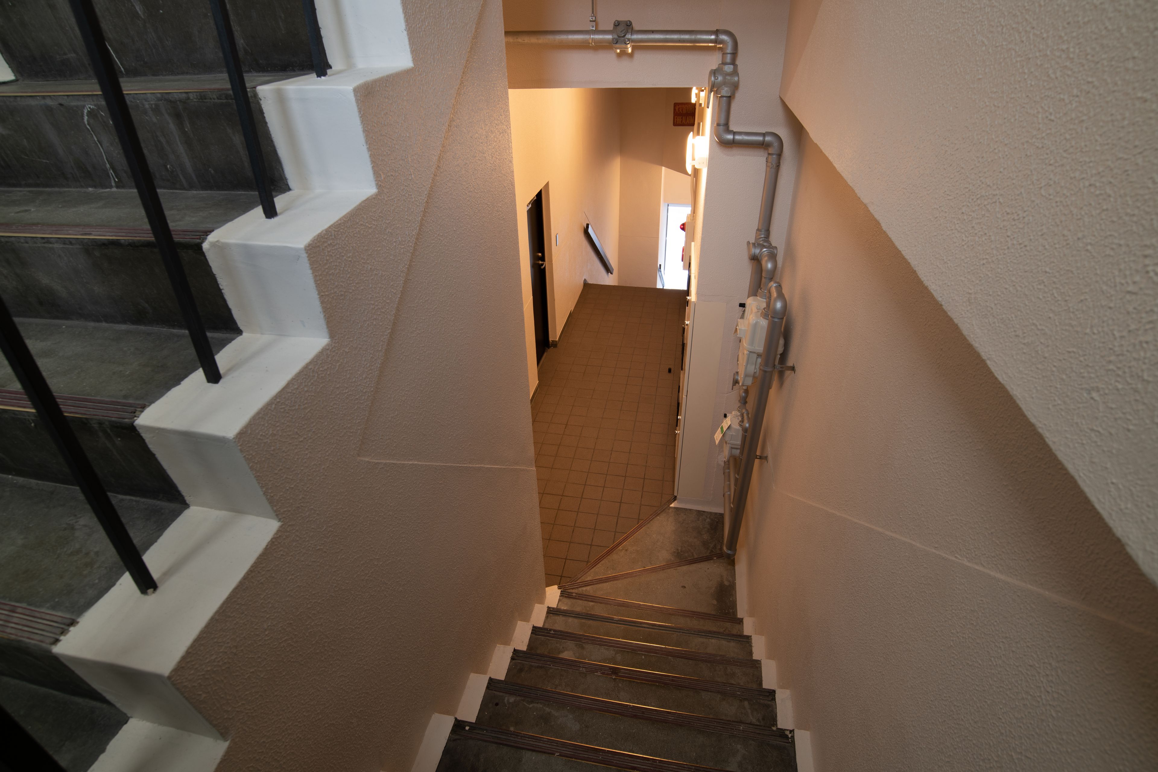 A staircase with a handrail and a tiled floor, leading to a room with a door and a light fixture.