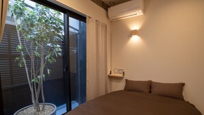 Un dormitorio con una cama grande, una planta en maceta, una ventana con cortinas y un aire acondicionado de pared.