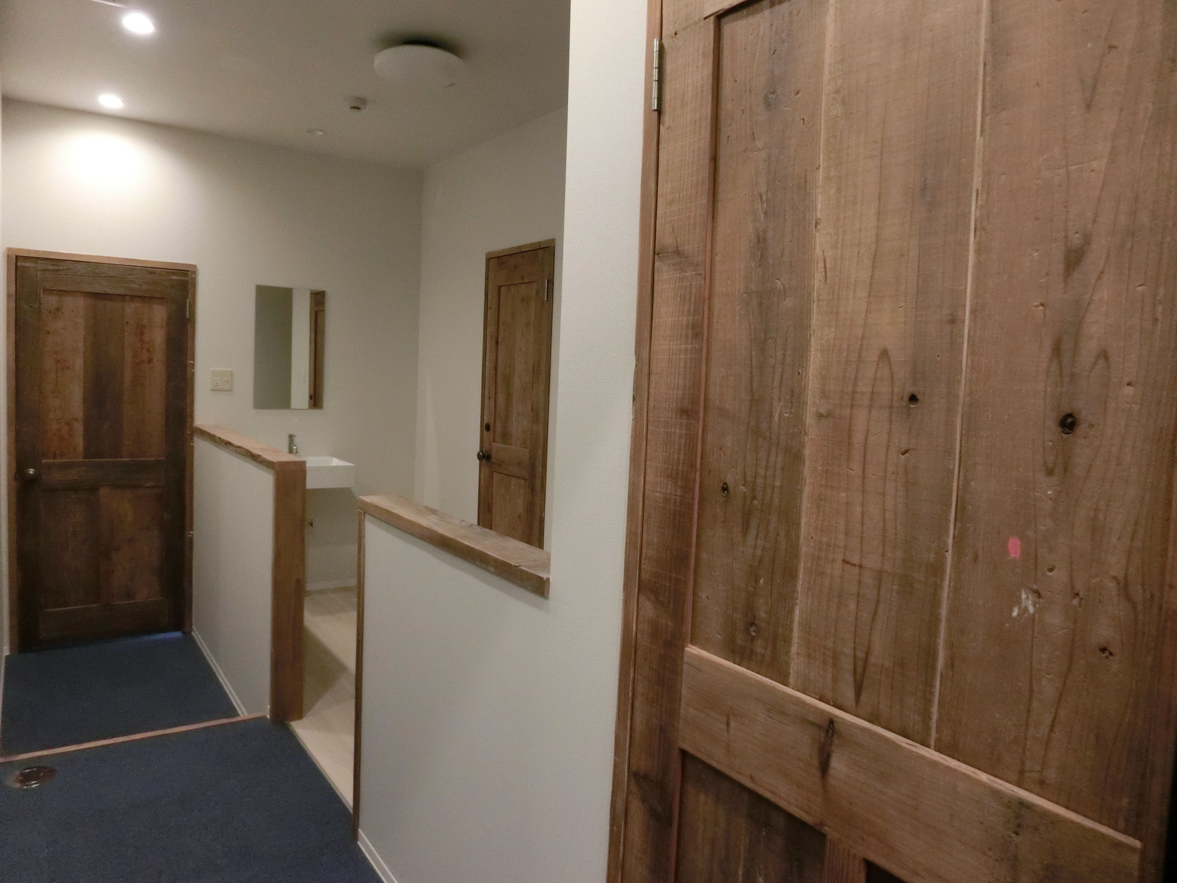 Un couloir avec des portes en bois, un mur blanc et une moquette bleue.