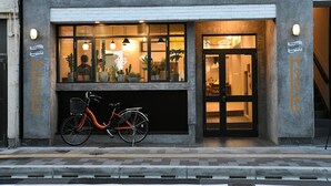 Cafetería de una casa de huéspedes con una bicicleta estacionada afuera, una entrada visible y una escalera que lleva al piso superior.