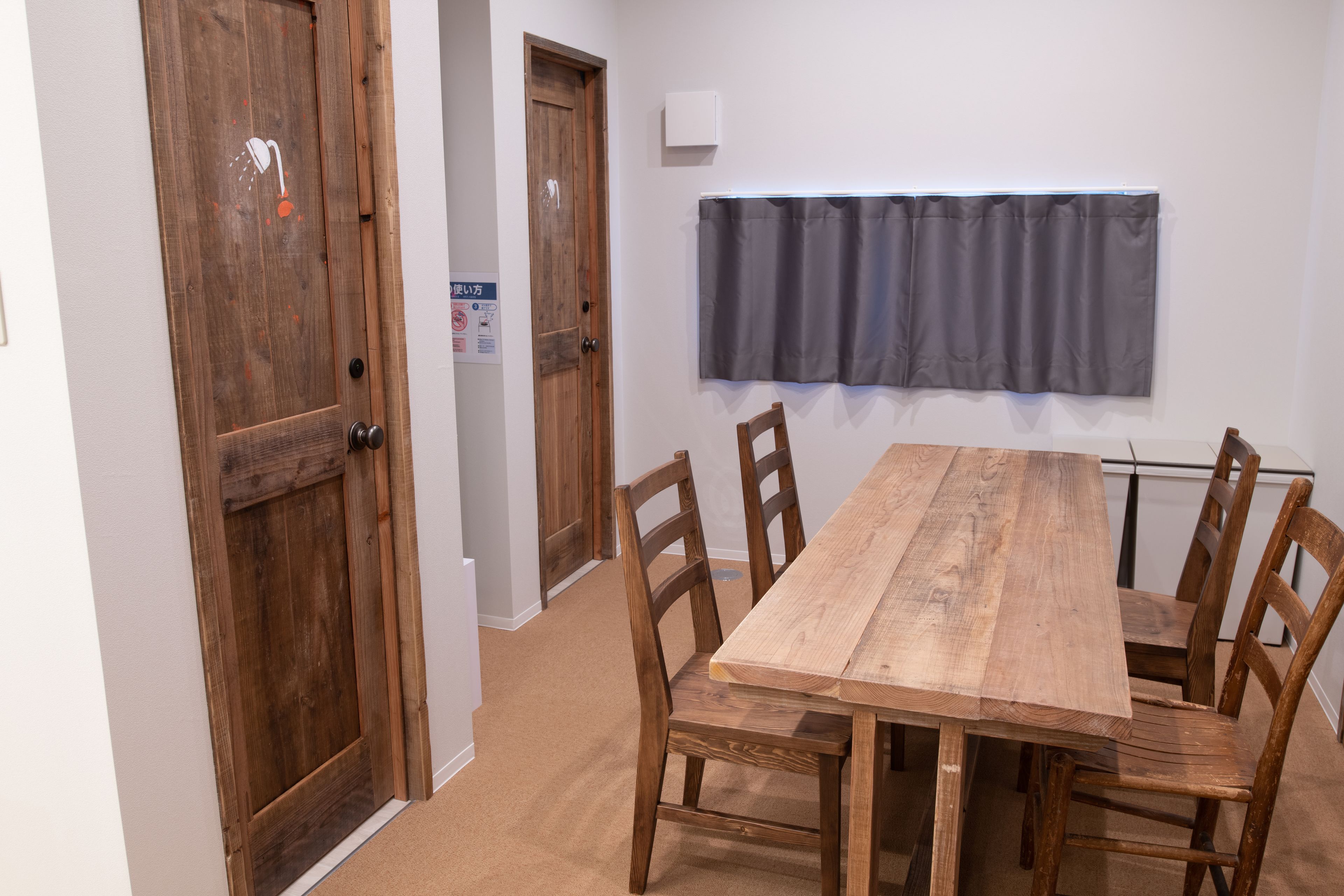 Una mesa de comedor de madera con seis sillas, una cortina oscura y una puerta de madera con un icono de ducha.