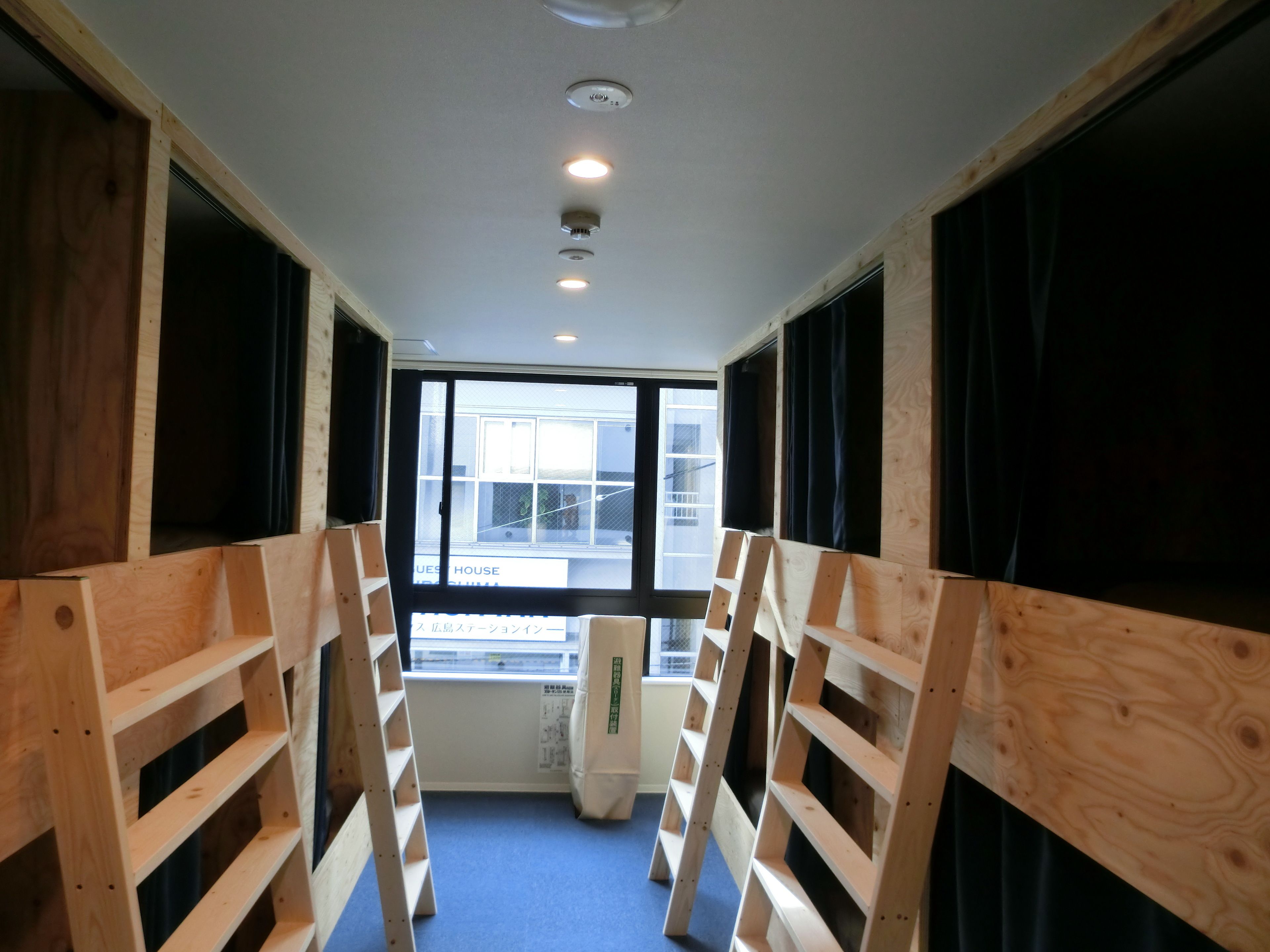 A room with bunk beds, a window with a view of a building, and a ceiling with recessed lighting.