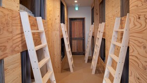 Un pasillo interior de madera con varias escaleras blancas apoyadas en las paredes, una puerta de madera al final y un interruptor de luz en la pared.