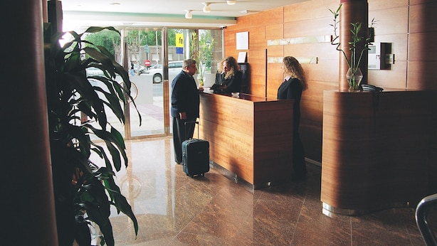Zona de recepción con un escritorio de madera, una planta en maceta y una puerta de vidrio que da al exterior.