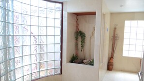 Una habitación con un ventanal grande, un rincón pequeño con una planta y suelo de baldosas.