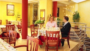 Un comedor con sillas y mesas de madera, pilares rojos y una escalera con barandilla metálica.
