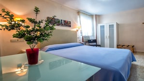 Una habitación de hotel con cama, escritorio con un jarrón rojo, un cuadro en la pared y un armario.