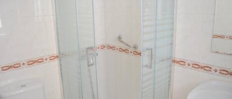 Un baño con ducha acristalada, inodoro y lavamanos.