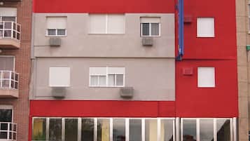 Un hotel de varios pisos con fachada roja y color beige, ventanas amplias y una entrada visible con un letrero.